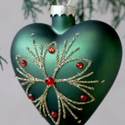A zöld üveg szívdísz arany csillámos mintájának és piros díszköveinek közeli részlete.