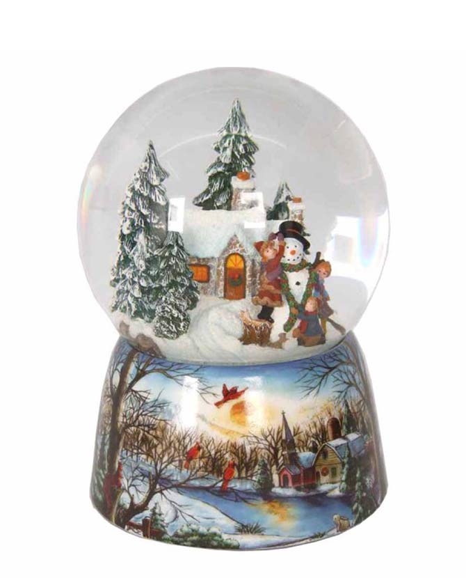 Karácsonyi zenélő-forgó hógömb, téli házikó előtt hóembert építő gyerekekkel.
