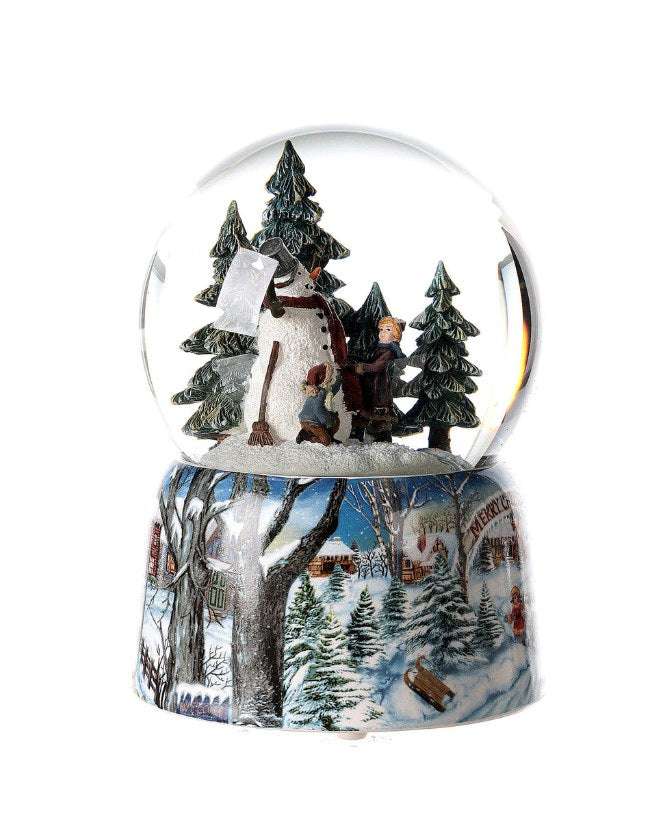 Karácsonyi zenélő-forgó hógömb, téli havas erdőben hóembert építő gyerekekkel.