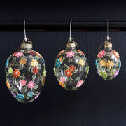 Plasztikus virágokkal díszített, függeszthető húsvéti üvegtojás.