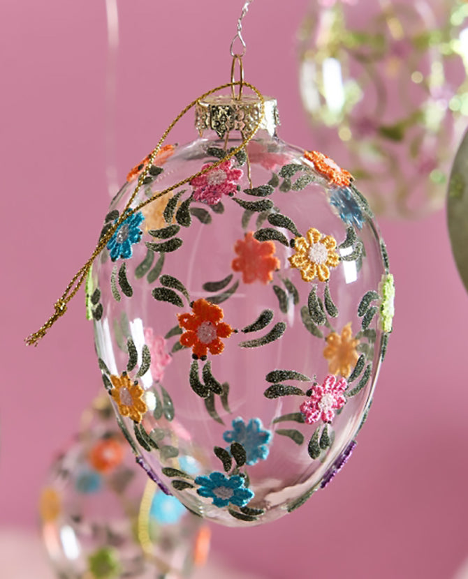 Plasztikus virágokkal díszített, függeszthető húsvéti üvegtojás.