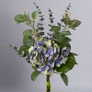 Kék és zöld árnyalatú mű hortenzia csokor szürke háttér előtt, elegáns zöld lombozattal.