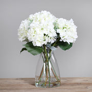 Víztiszta üvegvázában kialakított, krémszínű mű hortenzia virágcsokor.