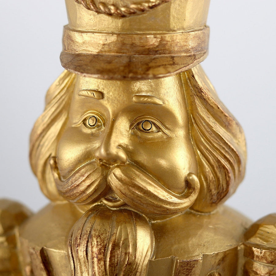 Arany színárnyalatú, faragott fahatású karácsonyi diótörő figura.