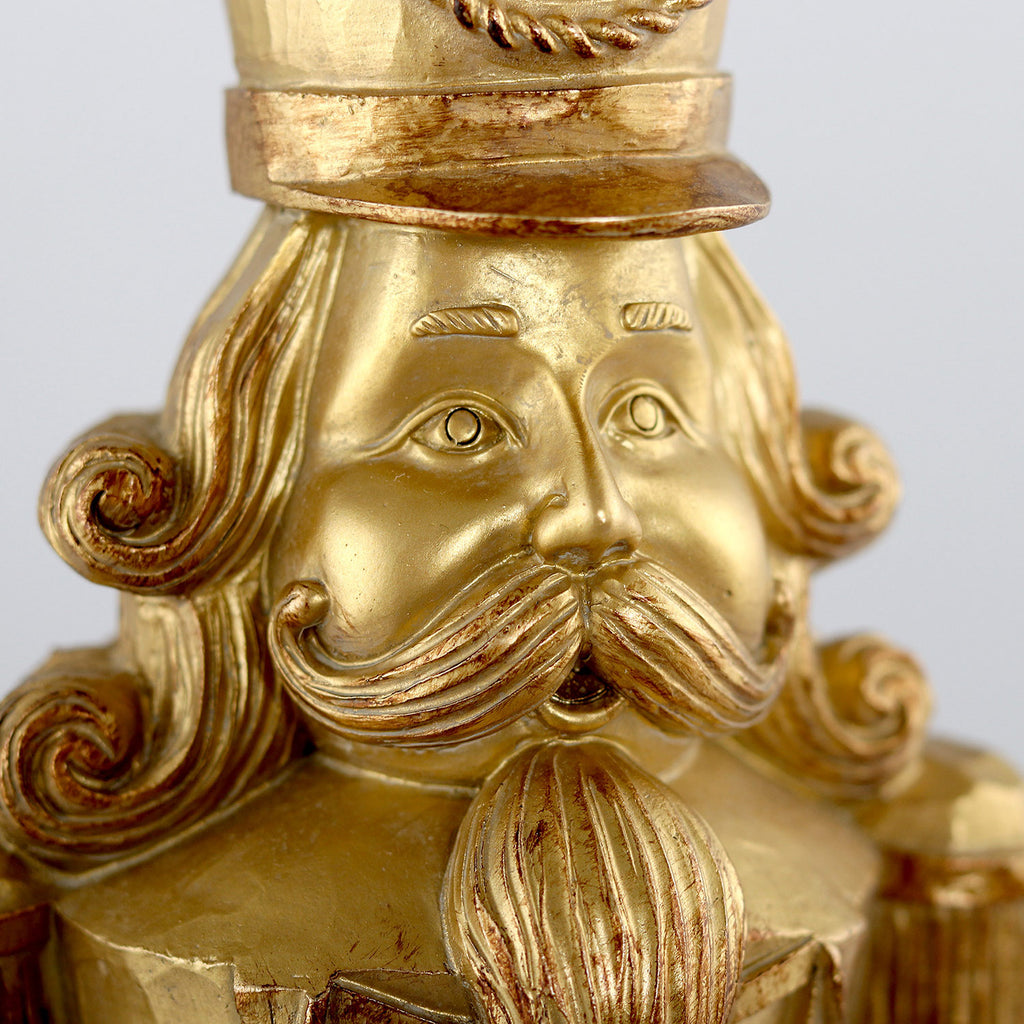 Arany színárnyalatú, faragott fahatású karácsonyi diótörő figura.