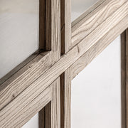 Közelkép a vitrinszekrény kereszteződő fa kereteiről és üvegfelületéről.