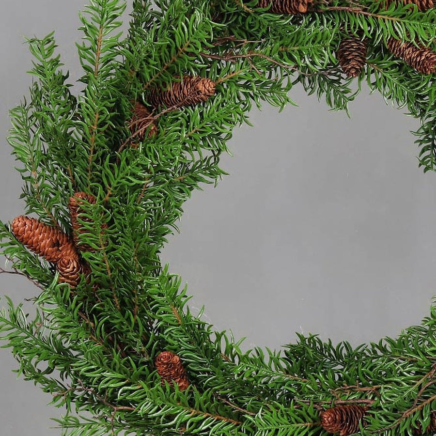 Mesterséges nobilis fenyőágakból készült, tobozokkal díszített ajtódísz koszorú.