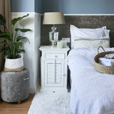 Fehér akácfa éjjeliszekrény modern hálószobában, textíliákkal és lámpával