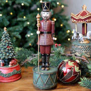 NOÉL zenélő karácsonyi diótörő figura ünnepi környezetben, karácsonyfa mellett