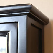 Díszesen megmunkált felső párkány a fekete faliszekrény sarkán, klasszikus formavilágban.