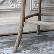 A bárszék lábrésze és hajlított lábtartója közelről, rusztikus padlón