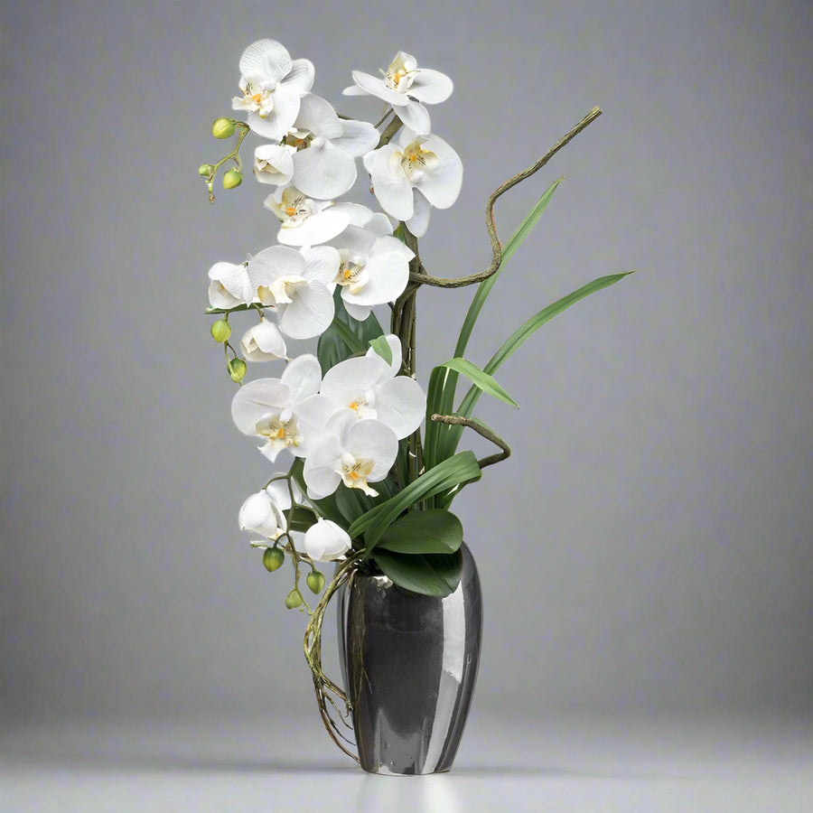 Fehér mű orchidea kompozíció ezüstszürke kaspóban, 68 cm magas.