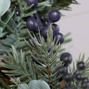 Fenyőág és kék bogyós részlet közelről a koszorún.