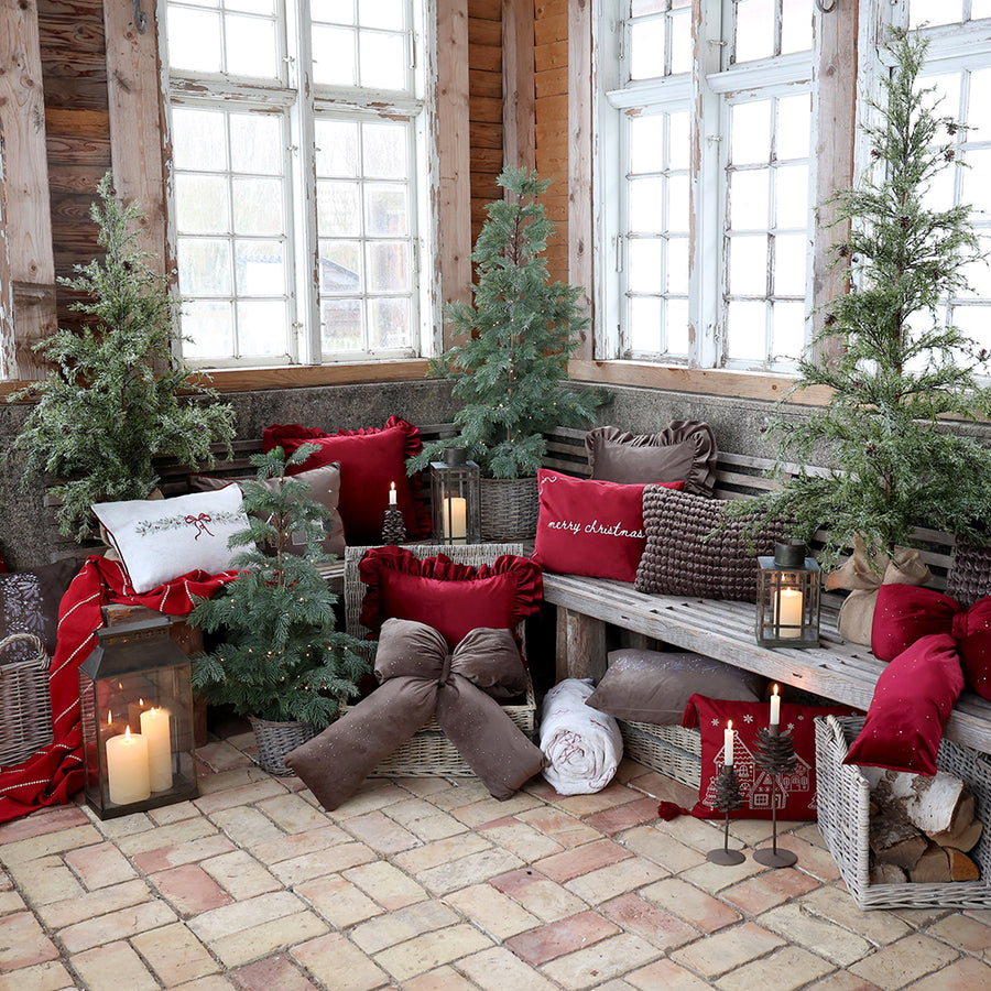 Havas hatású PINE műfenyő nagy ablak mellett, karácsonyi párnákkal díszített padnál