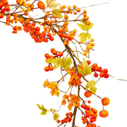 Közelkép őszi mű girlandról, piros bogyókkal és sárguló levelekkel.