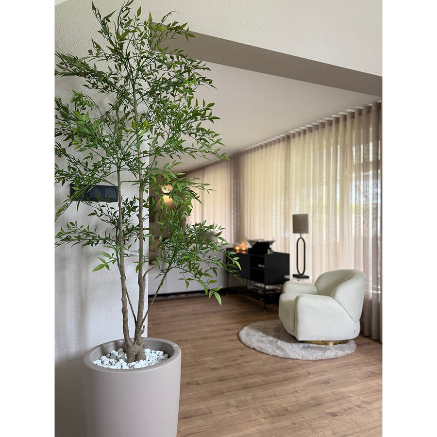 Élethű mű ruszkusz szürke kaspóban fehér kavics dekorral, modern nappali belső térben.