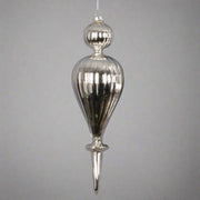 Egy ezüst, csepp formájú, bordázott üveg karácsonyfadísz közelről.