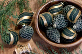 Olívazöld-arany Shiny üvegdíszek sötétzöld, rácsmintás díszekkel egy fatálban, örökzöld ágak között.