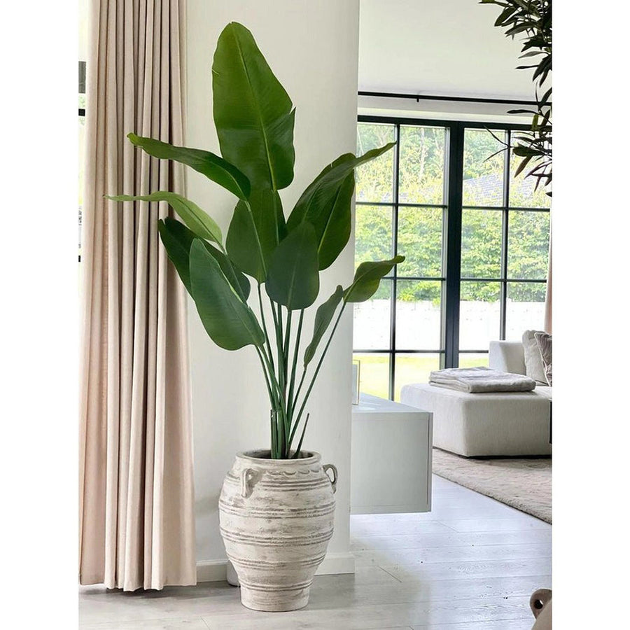 Élethű zöld strelitzia műnövény nappaliban, modern kaspóban elhelyezve