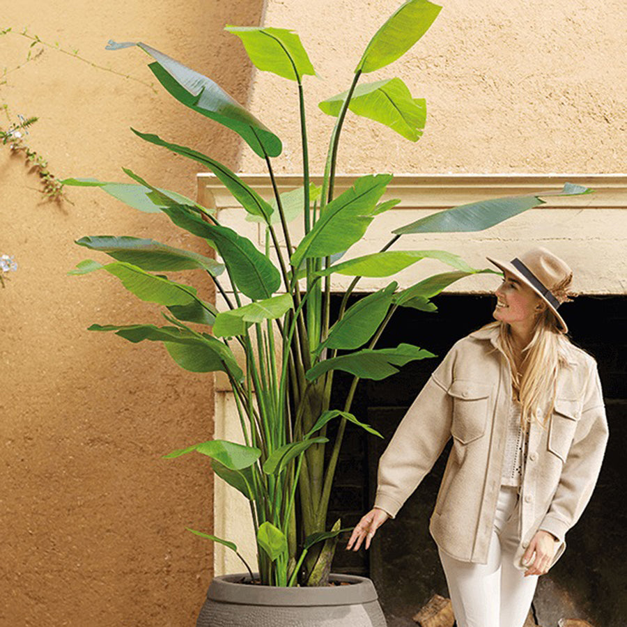 Nagyméretű mű strelitzia nappali dekorációként, nő áll mellette a méretarány érzékeltetésére.