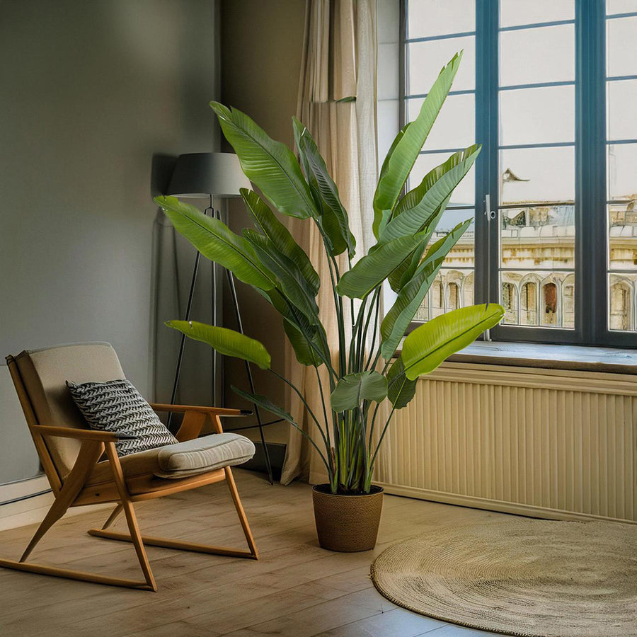 Élethű strelitzia műnövény modern nappali enteriőrben, ablak mellett elhelyezve.