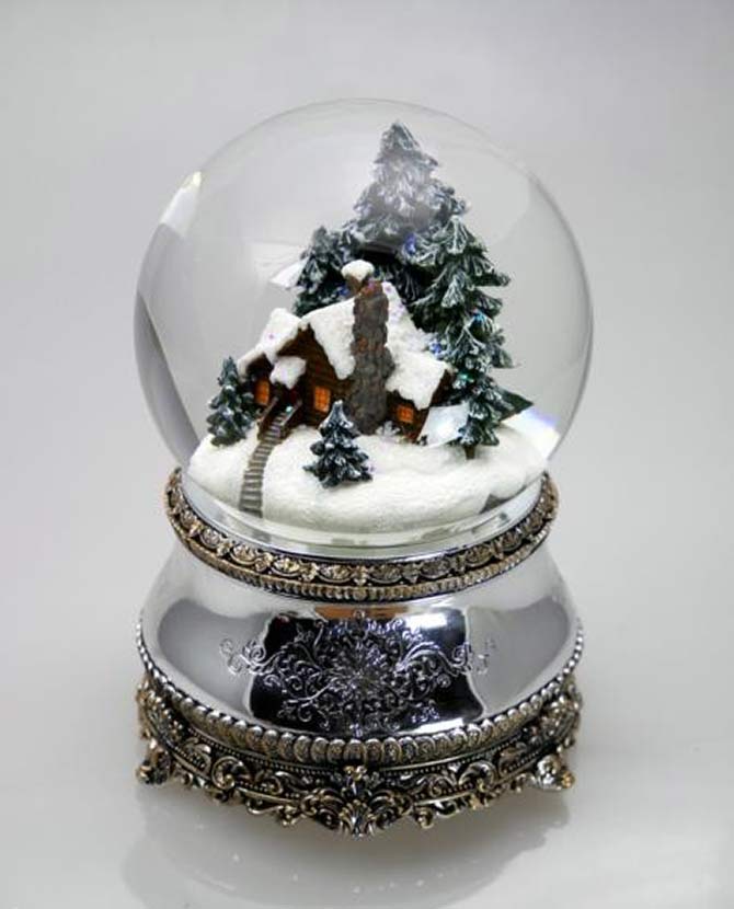 Karácsonyi zenélő-forgó hógömb, téli havas erdőben megbújó kunyhóval .
