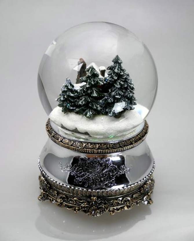 Karácsonyi zenélő-forgó hógömb, téli havas erdőben megbújó kunyhóval .