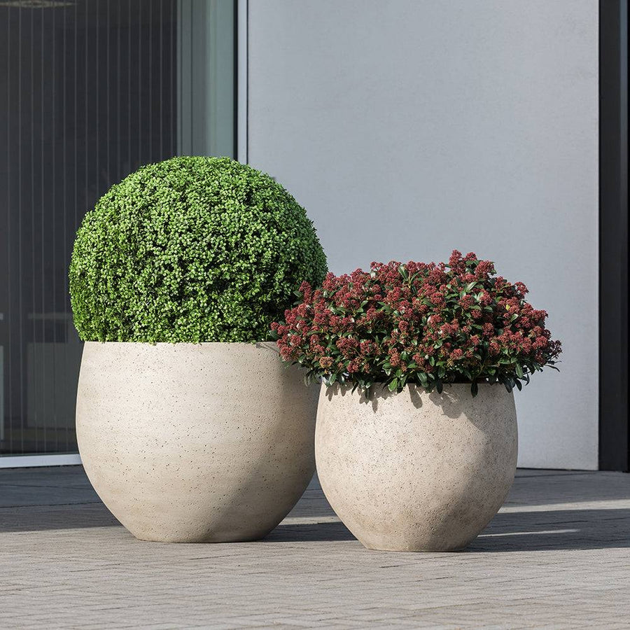 Betonhatású kaspók kültéren, modern épület előtt, zöld és piros növényekkel beültetve – Pottery Pots Urban kollekció