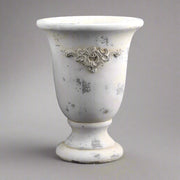 Vintage stílusú, talpas cement kaspó közelről, patinás krémszínű felülettel és plasztikus díszítéssel.