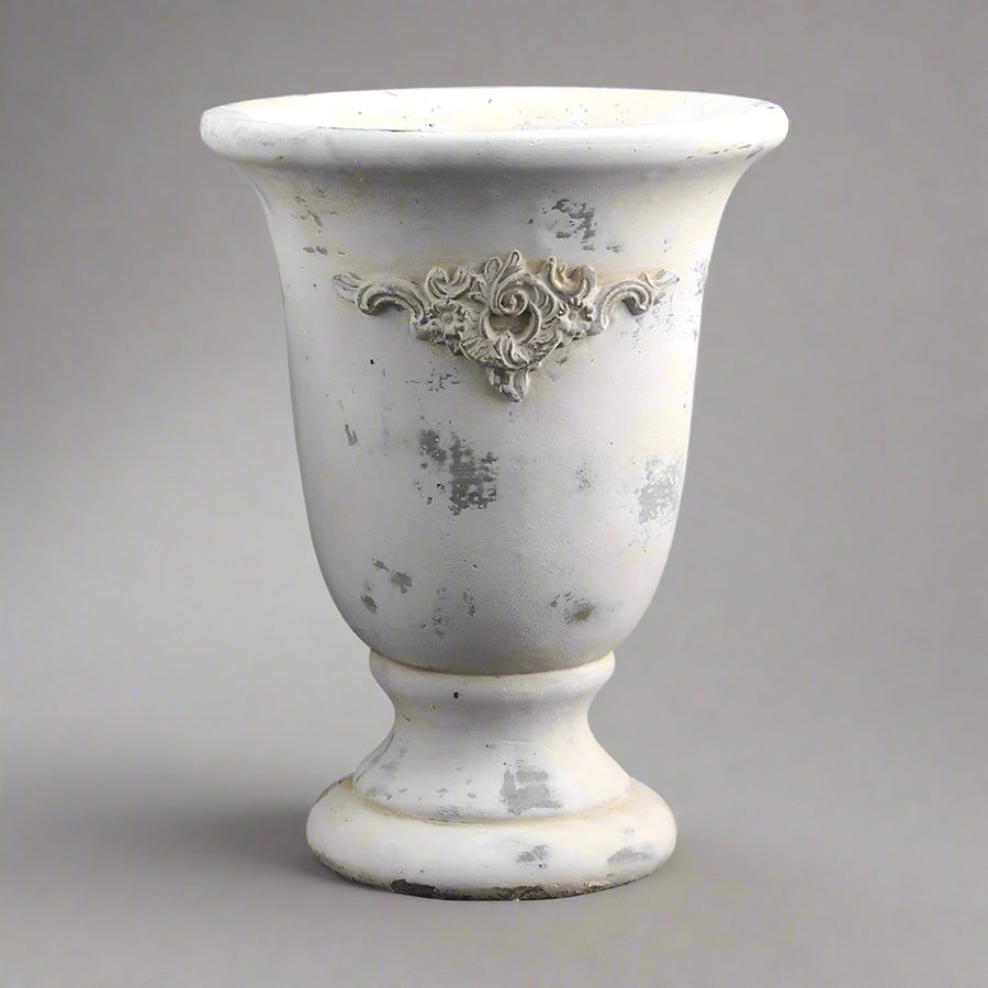 Vintage stílusú, talpas cement kaspó közelről, patinás krémszínű felülettel és plasztikus díszítéssel.