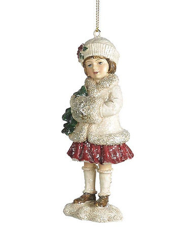Kezében kis fenyőfát tartó, krémszínű téli kislány formájú karácsonyfadísz.