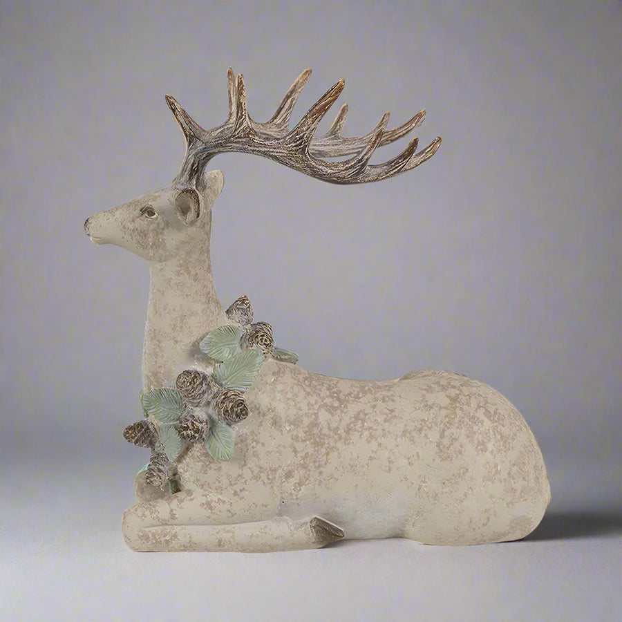 Tobozkoszorúval díszített, bézs színű, karácsonyi szarvas figura.
