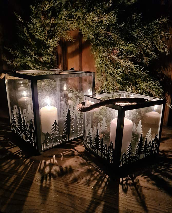 Vidéki rusztikus stílusú, antikolt szürke színű 2 darabos karácsonyi sziluettes fém lámpásszett fenyőkoszorú előtt antikolt fa deszkaasztalon
