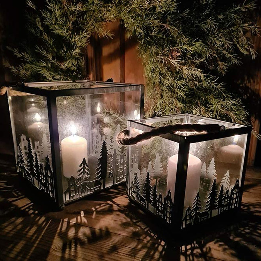 Vidéki rusztikus stílusú, antikolt szürke színű 2 darabos karácsonyi sziluettes fém lámpásszett fenyőkoszorú előtt antikolt fa deszkaasztalon