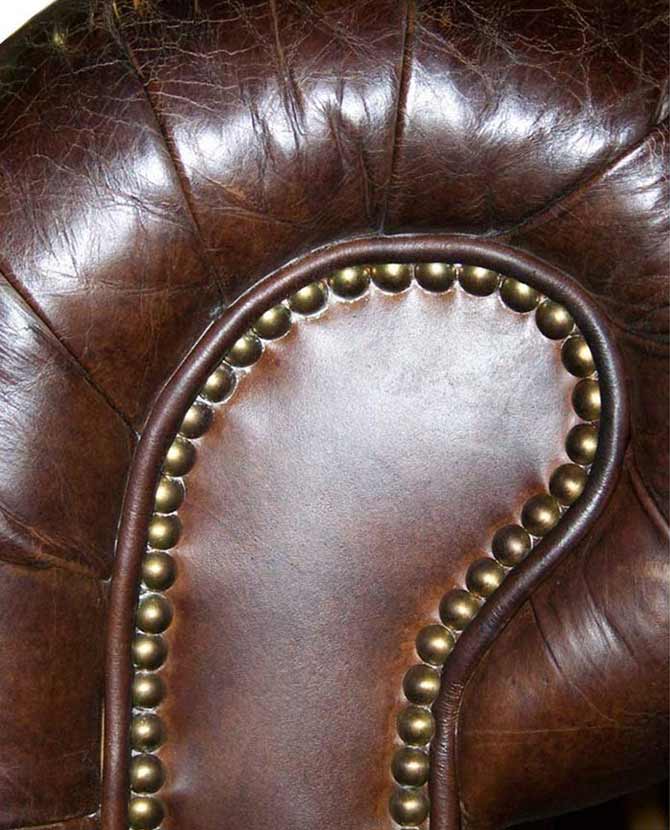 Klasszikus stílusú, bőrből készült Chesterfield kanapé szegecselt karfa részlete.