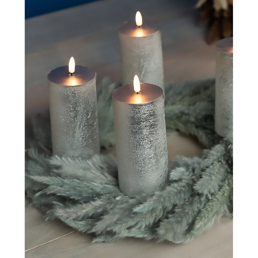 4 darabos, élethű megjelenésű, ezüstszínű, valódi viaszból kialakított, időzítővel rendelkező, távirányítós, dimmelhető, 15 cm magas LED oszlopgyertya, fenyőkoszorún.