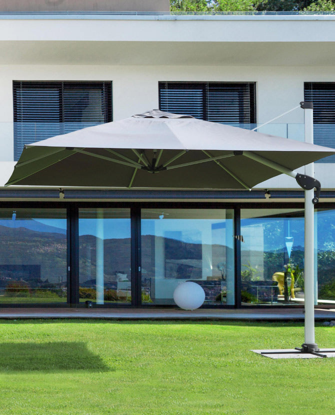 Modern stílusú épület füves udvarán álló fémvázas napernyő.