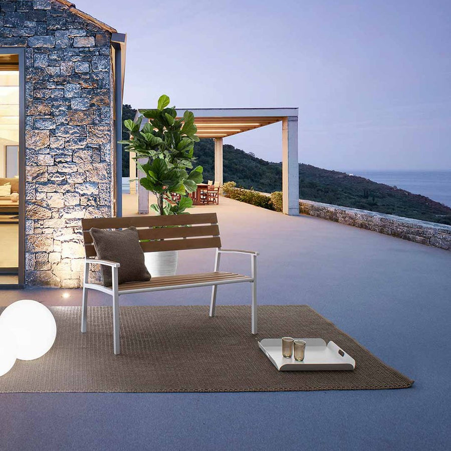 Teraszon álló fémvázas kerti pad rattan szőnyeggel, és dekorlámpával.