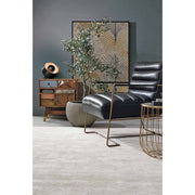 Loft stílusú nappaliban álló fekete műbőr fotel, kis momóddal és cserepes növénnyel.