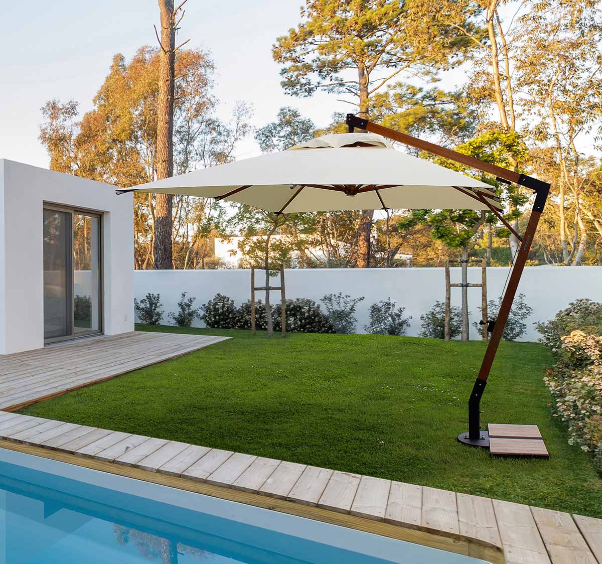 Füves udvaron, medence mellett álló teakfa vázas szövet napernyő.