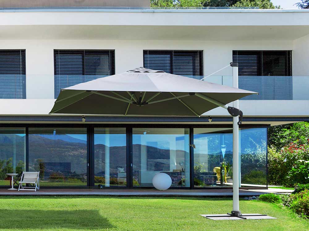Modern stílusú épület füves udvarán álló fémvázas napernyő..