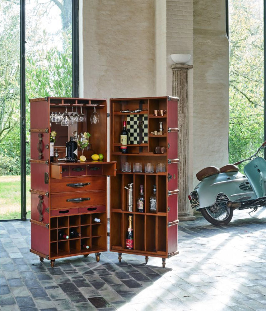 Fedett teraszon álló utazási bőrönd formájú bárszekrény poharakkal, italokkal, gyümölcsökkel.