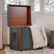 Hálószobában álló nyitott fedelű utazóláda kisasztal, takaróval.