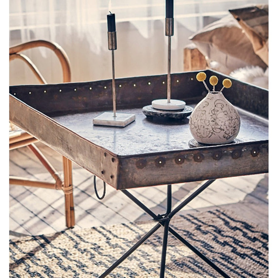 Loft stílusú szobában álló fém kisasztal fém gyertyatartóval.