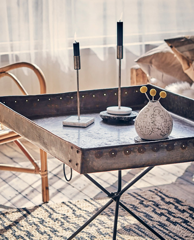 Loft stílusú szobában álló fém kisasztal fém gyertyatartóval.