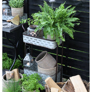 Hangulatkép: a görgős virágállvány egy teraszon, rajta növények, kaspók, lámpások.