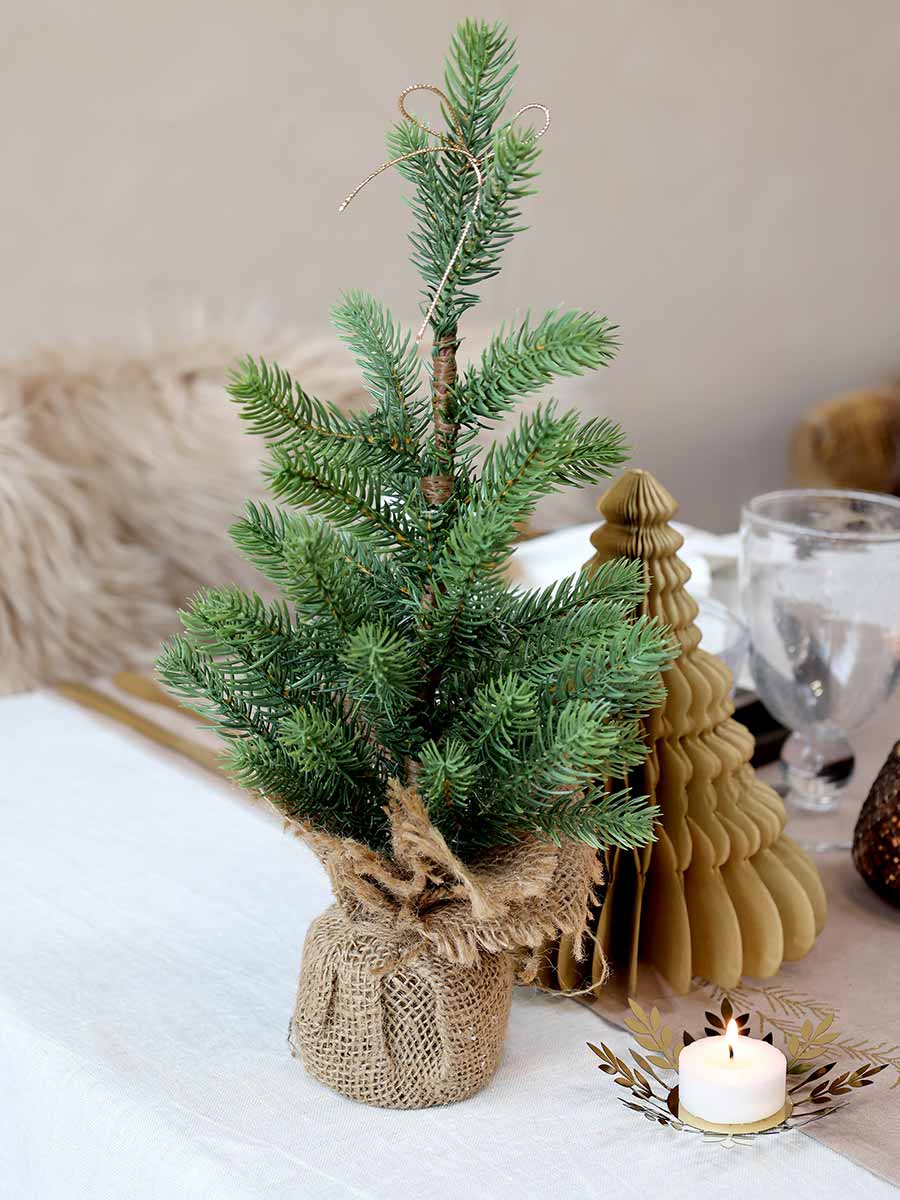 Karácsonyi asztalt díszítiő, élethű, kisméretű deko fenyőfa jutazsákban.