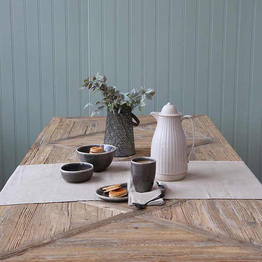 Fenyőfából készült X-lábú étkezőasztal délutáni teához terítve.