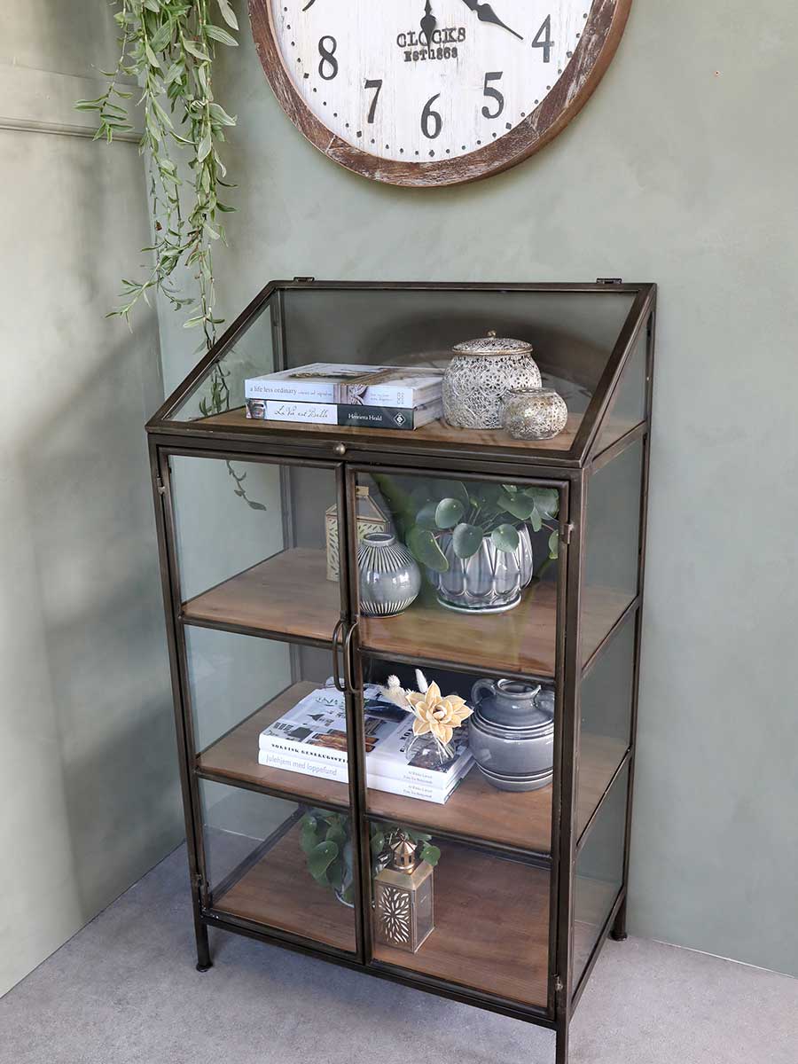 Könyvekkel, kerámiákkal és növényekkel megpakolt ipari stílusú vitrines tárolószekrény.
