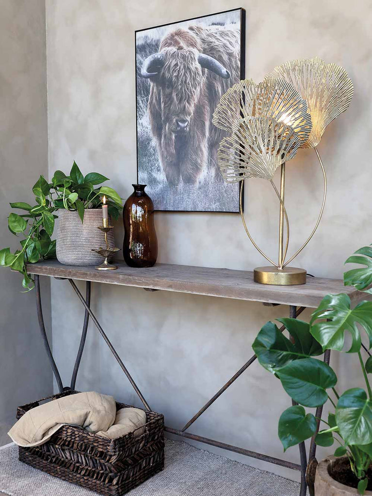 Glamour stílusú, antikolt rézszínű, fémből készült, páfrányfenyő leveleket mintázó asztali lámpa vidéki stílusú nappaliban.